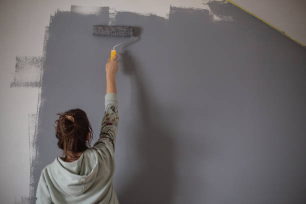 Человек красит стену в серый цвет с помощью малярного валика.