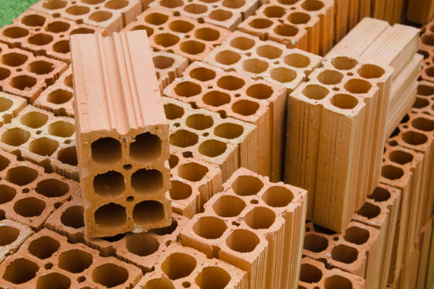 Стопки новых красных глиняных кирпичей с отверстиями, использованных для строительства и строительства, аккуратно разложены на деревянной палитре.